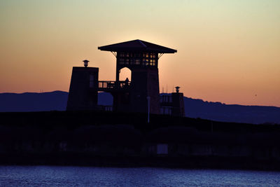 Silhouette building by sea against sky during sunset