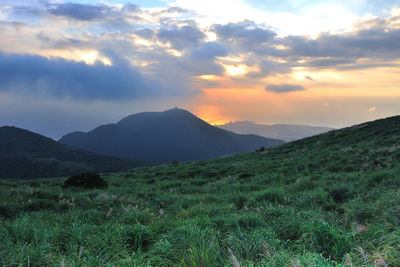 Scenic view of landscape against cloudy sky during sunset