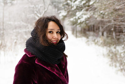 Smiling woman with long brown hair in a coat from faux fur on a background of winter forest.