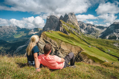 Rear view of people sitting on mountain against sky