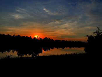 Silhouette trees by lake against sky during sunset