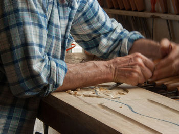 Midsection of male carpenter carving wood in workshop