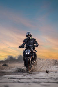 Man riding motorcycle on land against sky during sunset