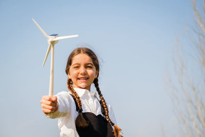 Portrait of young woman with arms raised standing against sky