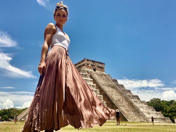 Low angle view of tourists standing by historical building against sky