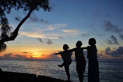 Silhouette people on beach against sky during sunset