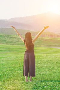 Rear view of woman with arms raised standing on field