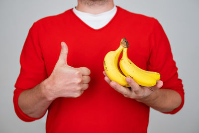 Midsection of woman holding banana against white background