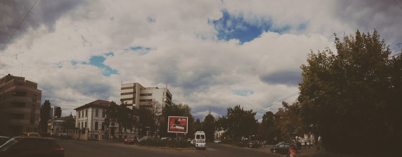 transportation, car, land vehicle, mode of transport, road, sky, street, cloud - sky, tree, building exterior, road marking, architecture, the way forward, built structure, cloudy, cloud, road sign, on the move, city, outdoors