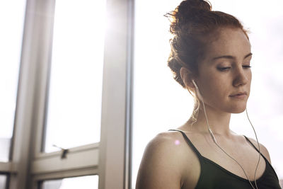 Low angle view of thoughtful woman listening music while standing by window