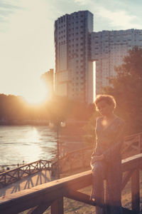 Woman sitting on railing in city during sunset