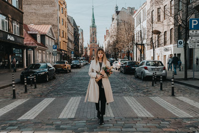 Portrait of young woman standing on road in city