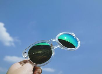 Cropped image of hand holding sunglasses against sky