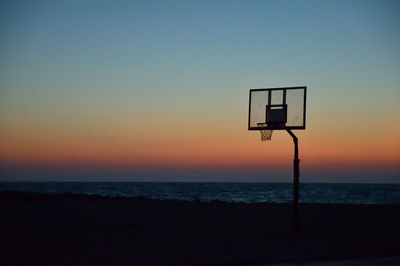 Silhouette basketball hoop at beach against sky during sunset