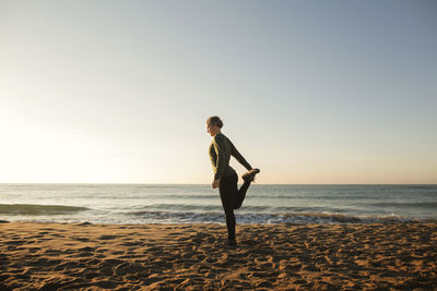 Full length of woman doing yoga at beach against clear sky