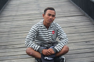 Young man looking away while sitting on pier