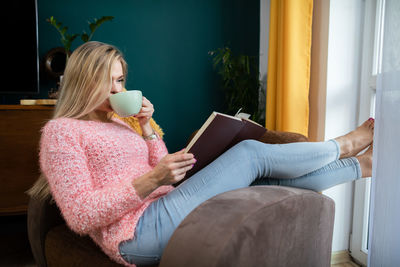 A girl relaxes by reading a book and drinking coffee.