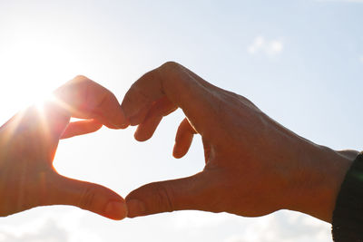 Cropped hands making heart shape against sky