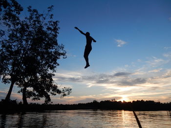 Silhouette man jumping in lake against sky during sunset