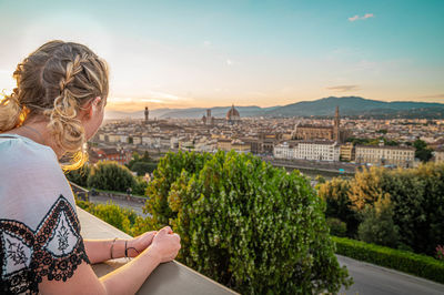 Man sitting by cityscape against sky during sunset
