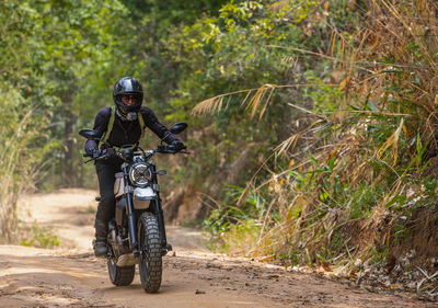 Woman riding her scrambler type motorcycle through forrest