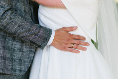 Groom's hand with the wedding ring lies on the bride's waist person