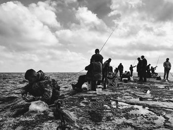 People fishing at beach against sky
