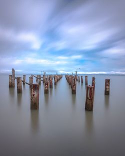 Weathered wooden posts amidst sea against sky