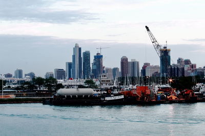 Boats in harbor by buildings against sky in city