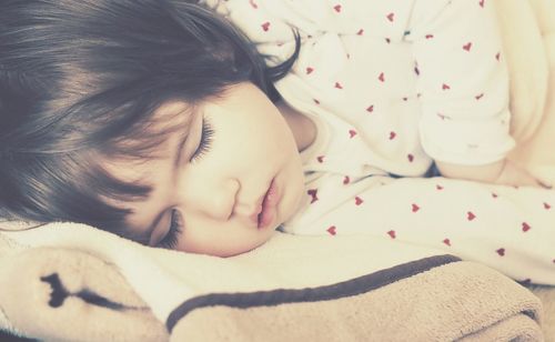 Side view of cute baby girl sleeping on bed at home