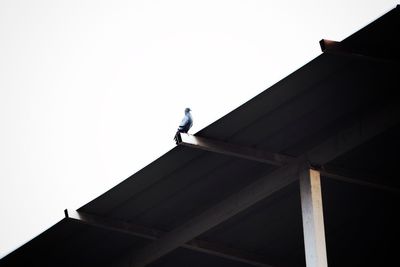 Low angle view of man standing on roof against sky