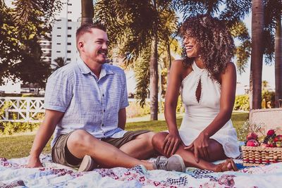 Happy couple talking while sitting on picnic blanket at park