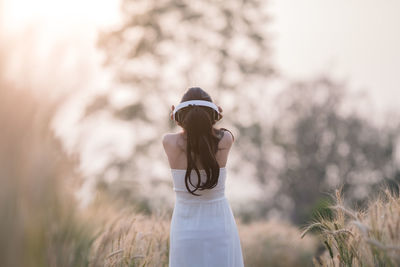 Rear view of woman using headphones while listening music on field during sunset