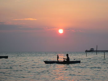 Silhouette people in boat on sea against sky during sunset