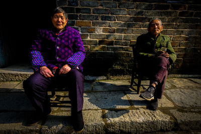 Full length of an old couple sitting against wall