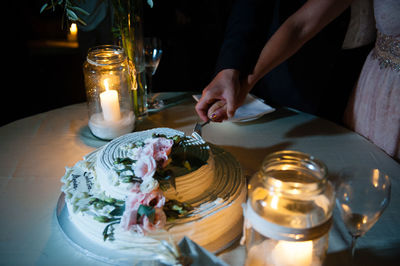 Midsection of couple cutting wedding cake