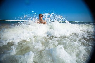 Man splashing water in sea against blue sky