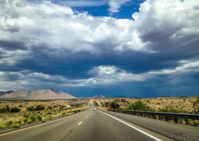 Road along landscape against cloudy sky