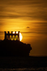 Silhouette rocks by sea against sky during sunset