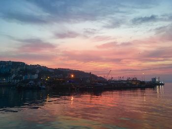Scenic view of sea by buildings against sky at sunset