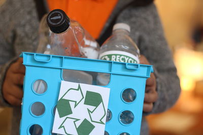 Midsection of person holding basket with plastic bottles