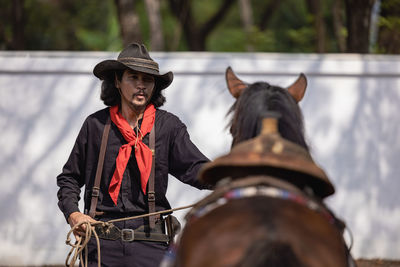 In an outdoor barn, one man dressed as a cowboy trains his horse to run in a circle around him.