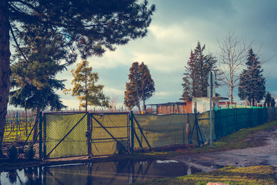 Fence by trees growing on field against sky