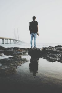 Rear view of silhouette man standing on bridge over sea