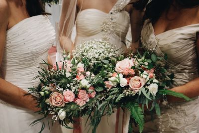 Midsection of bride with bridesmaid holding bouquet while standing in wedding ceremony