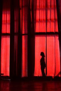 Side view of silhouette boy standing against red curtain