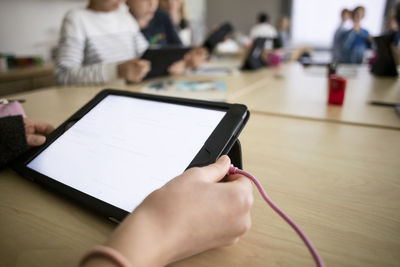 Cropped hand of child holding digital tablet in classroom