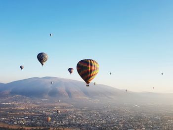 Hot air balloons flying in city against clear sky