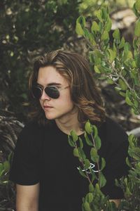 Handsome young man wearing sunglasses standing amidst plants