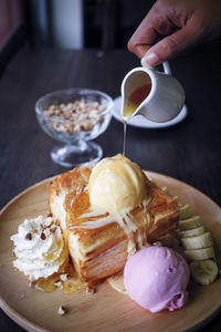 Cropped hand of woman pouring syrup on food in plate